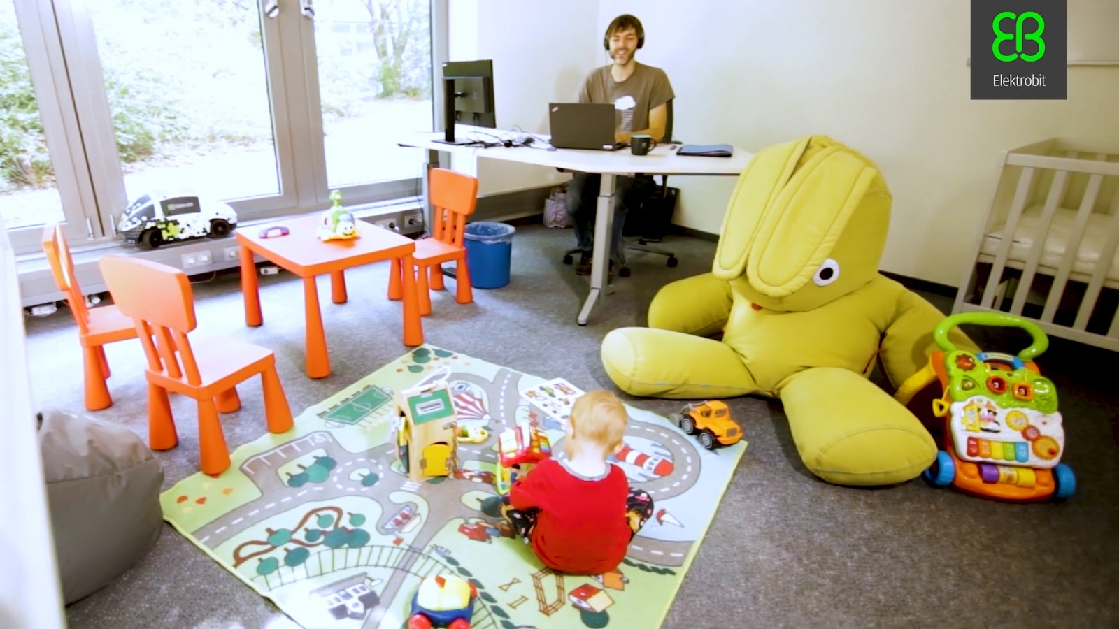 Ein Vater arbeitet in einem der hauseigenen Parent-Child-Offices, während sein Kind neben dem Schreibtisch spielt